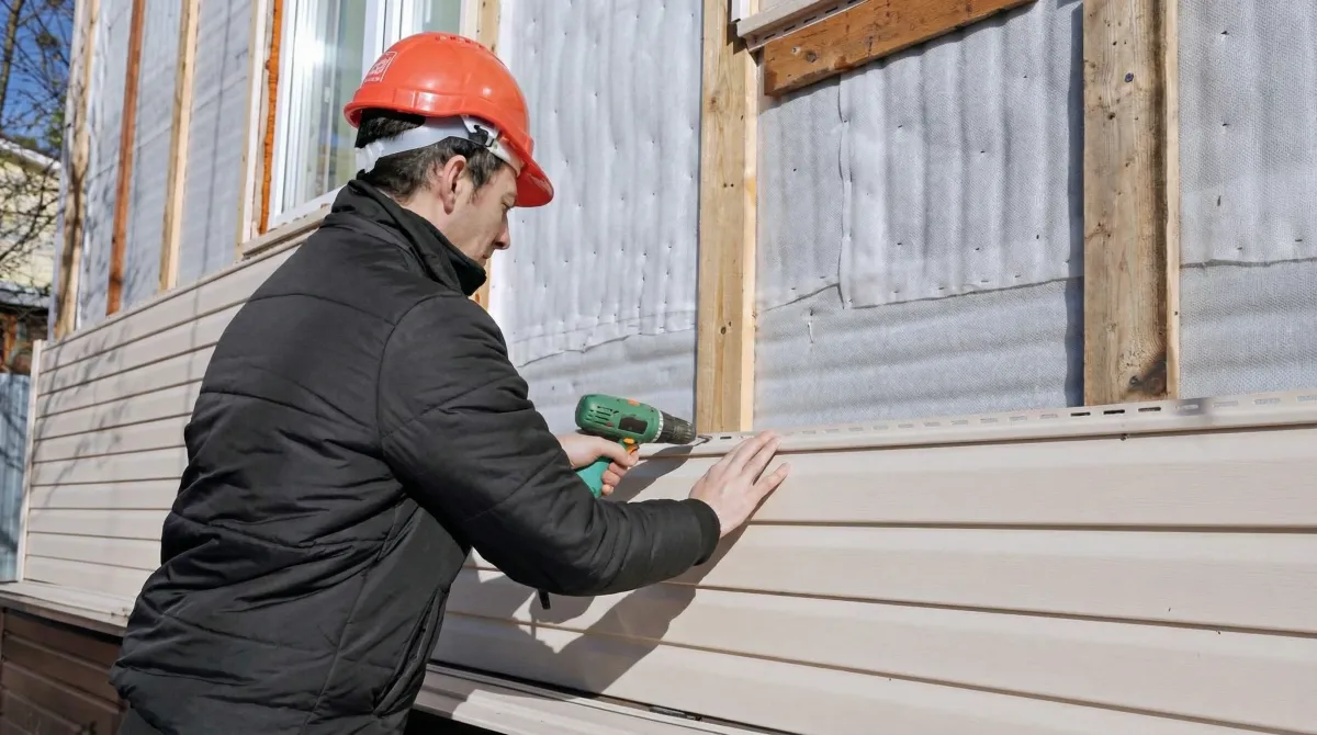 Siding replacement professional using a power drill to install new tan vinyl siding on a home exterior in Chattanooga, TN